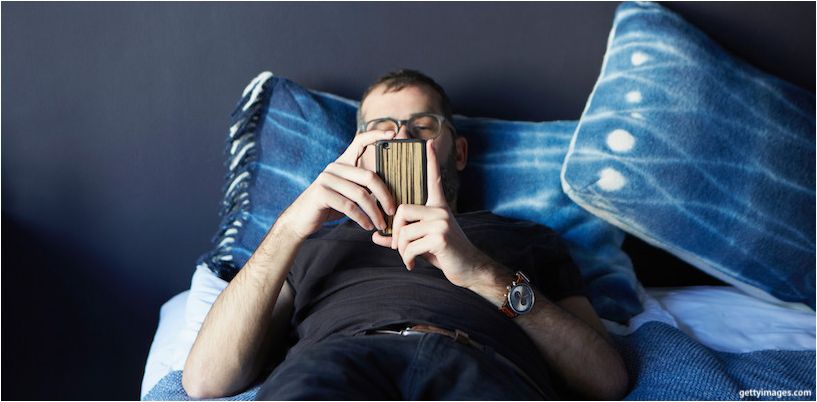 bărbat culcat pe pat și uitându-se la un smartphone