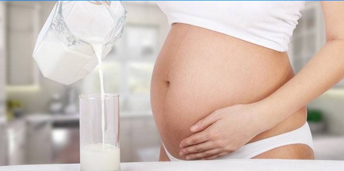 Femeia însărcinată toarnă lapte copt fermentat într-un pahar