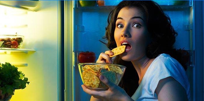 Fată care mănâncă biscuiti în fața unui frigider deschis