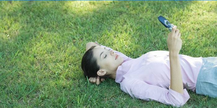 Fata se întinde pe iarbă cu un telefon