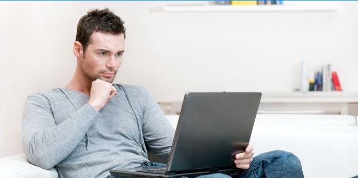 Un bărbat stă pe o canapea cu un laptop