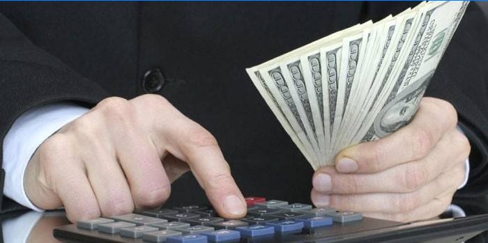 Un bărbat mizează pe un calculator și ține bancnote în mână