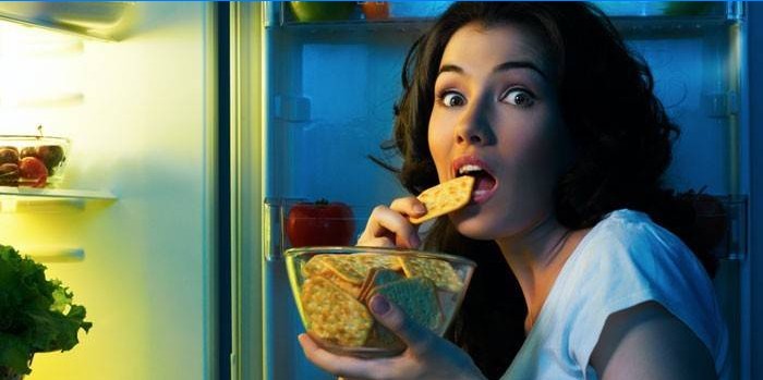 Fata din fața unui frigider deschis mănâncă biscuiti